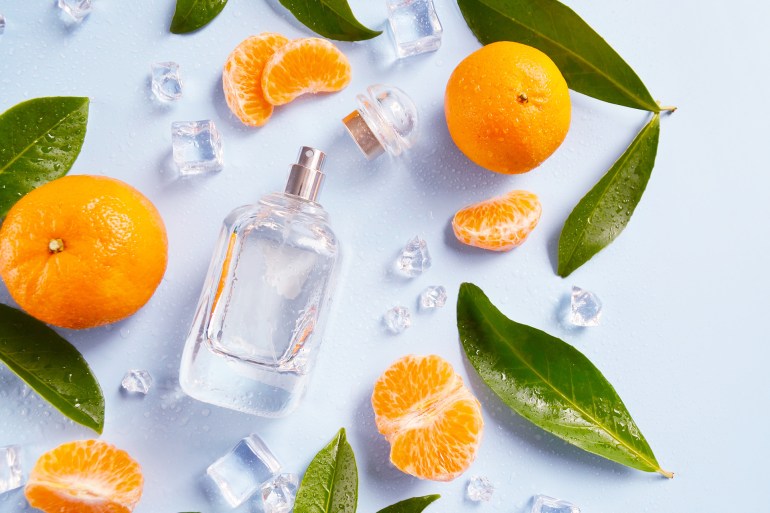 Glass bottle of perfume with oranges, green leaves, ice cubes, water drops on the light blue background. Smell of summer. Fresh orange cooling perfumery. Space for text.; Shutterstock ID 2057482436; purchase_order: ajanet; job: ; client: ; other: