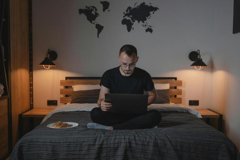 A Man Using a Laptop while Sitting on a Bed