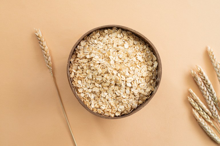 Oats or oat flakes in wooden bowl and golden wheat ears on beige background. Top view, horizontal. Healthy lifestyle, healthy nutrition, vegan food concept; Shutterstock ID 2427948055; purchase_order: aj net; job: ; client: ; other: