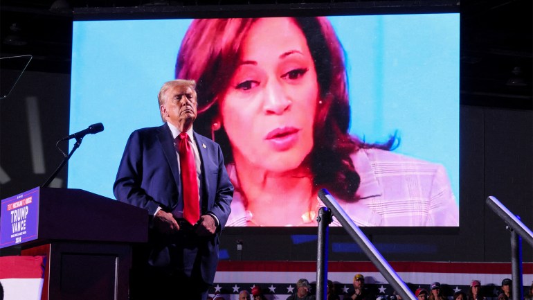 Republican presidential nominee and former U.S. President Donald Trump looks on as Democratic presidential nominee and U.S. Vice President Kamala Harris' face appears as a video plays on a screen, during a rally at Huntington Place in Detroit, Michigan, U.S. October 18, 2024. REUTERS/Brian Snyder