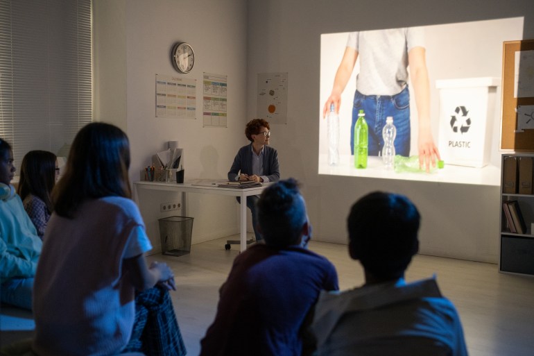 Schoolchildren watching video about recycling plastic bottles in dark classroom