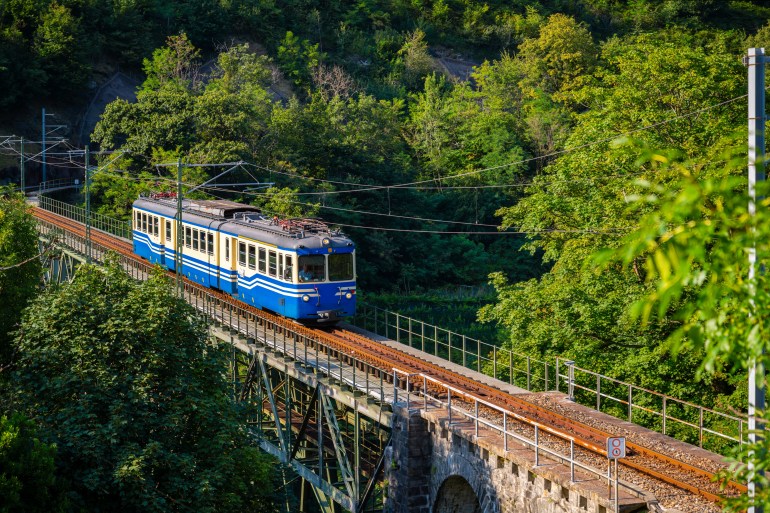 Historic electric train on famous steel bridge in Intragna in Centovalli valley. Famous narrow gauge railway line from Locarno to Domodossola in Italy in the Swiss Alps. Popular tourist train journey.; Shutterstock ID 2335373327; purchase_order: aljazeera ; job: ; client: ; other:Historic electric train on famous steel bridge in Intragna in Centovalli valley. Famous narrow gauge railway line from Locarno to Domodossola in Italy in the Swiss Alps. Popular tourist train journey.; Shutterstock ID 2335373327; purchase_order: aljazeera ; job: ; client: ; other: