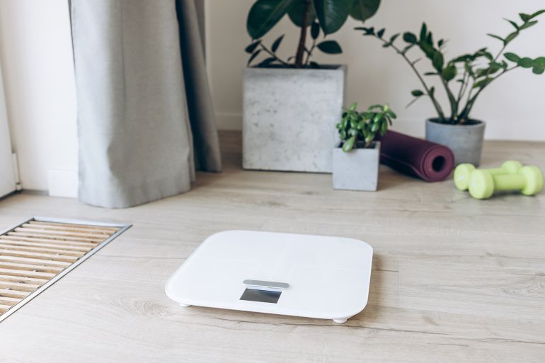 Fitness equipment and digital scale surrounded by green potted plants on a wooden floor, concept of home exercise and wellness decor - stock photo