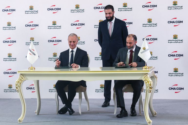 Syrian President Ahmed al-Sharaa (C) looks on as Joseph Dakak, the regional director of French shipping company CMA GGM, (L) and Latakia port director Ahmed Mustafa sign an agreement in Damascus on May 1, 2025.