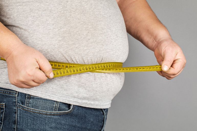 A man measures his fat belly with a measuring tape. on a gray background