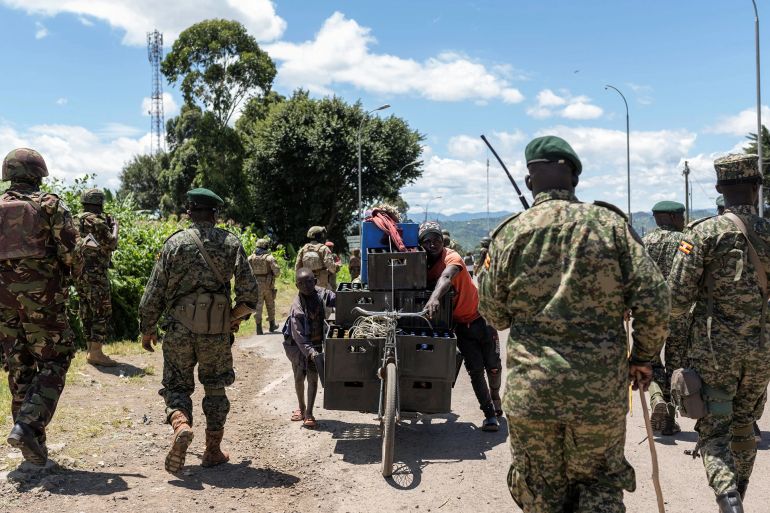 Ugandan soldiers walk near people pushing a bicycle loaded with goods, at the border post between Uganda and the Democratic Republic of the Congo [File: Arlette Bashizi/Reuters]