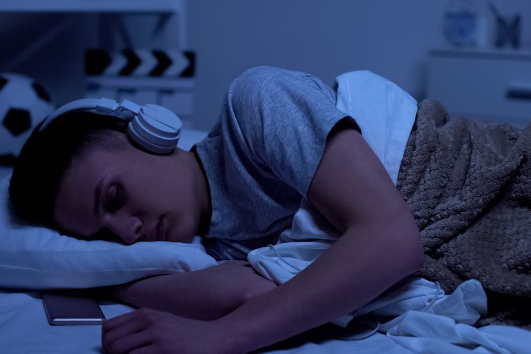 Male teenage boy fallen asleep in headphones, overworked student relaxing